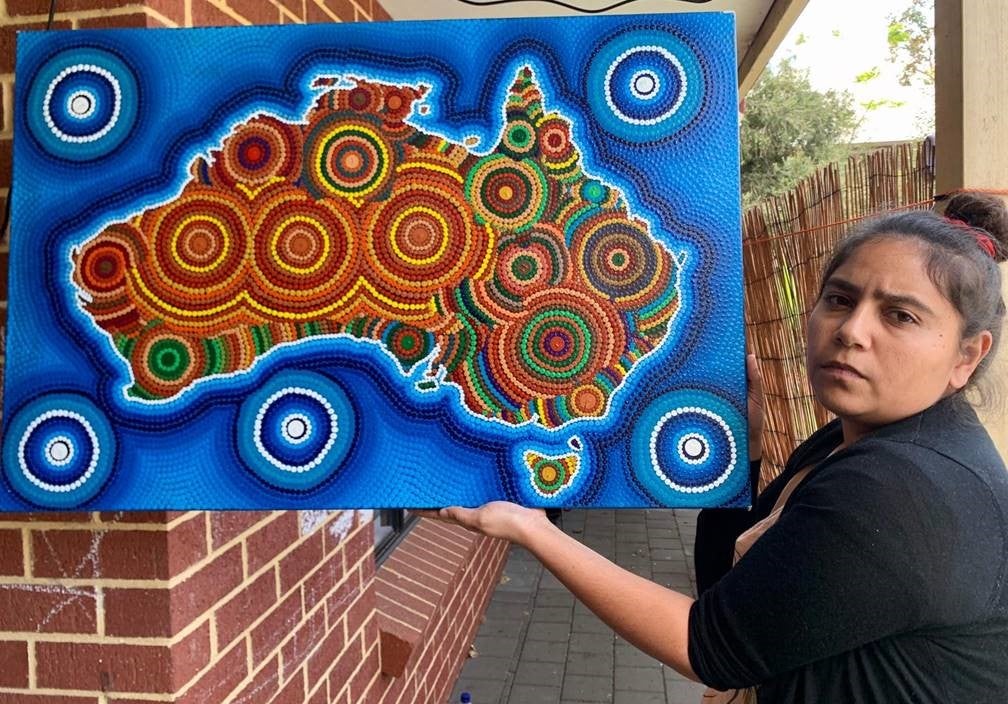 A woman holds up a colorful painting that depicts the Australian continent