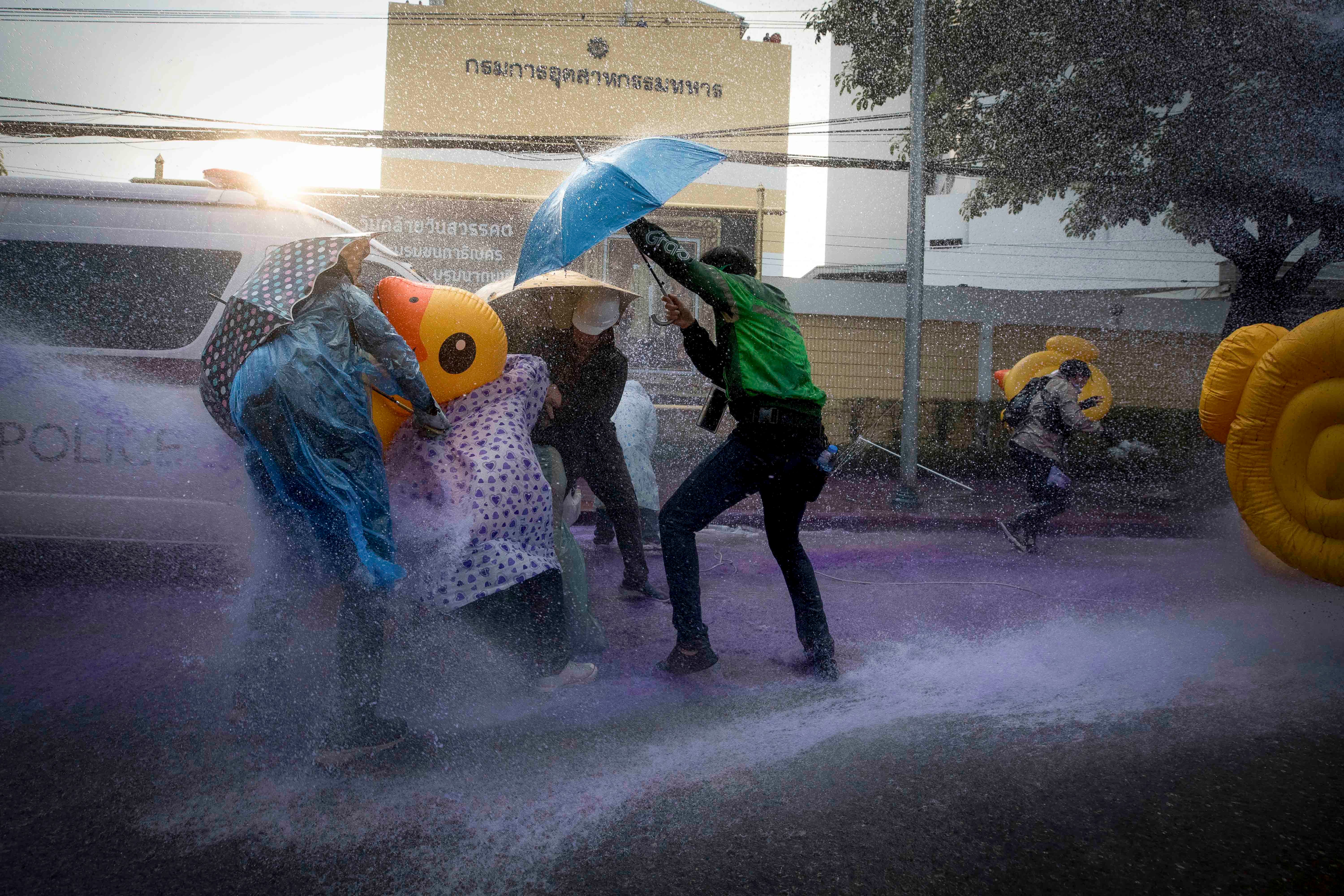 Democracy demonstrators take cover with inflatable ducks and umbrellas as police use water cannons during a protest rally near the parliament in Bangkok, November 17, 2020. © 2020 AP Photo/Wason Wanichakorn