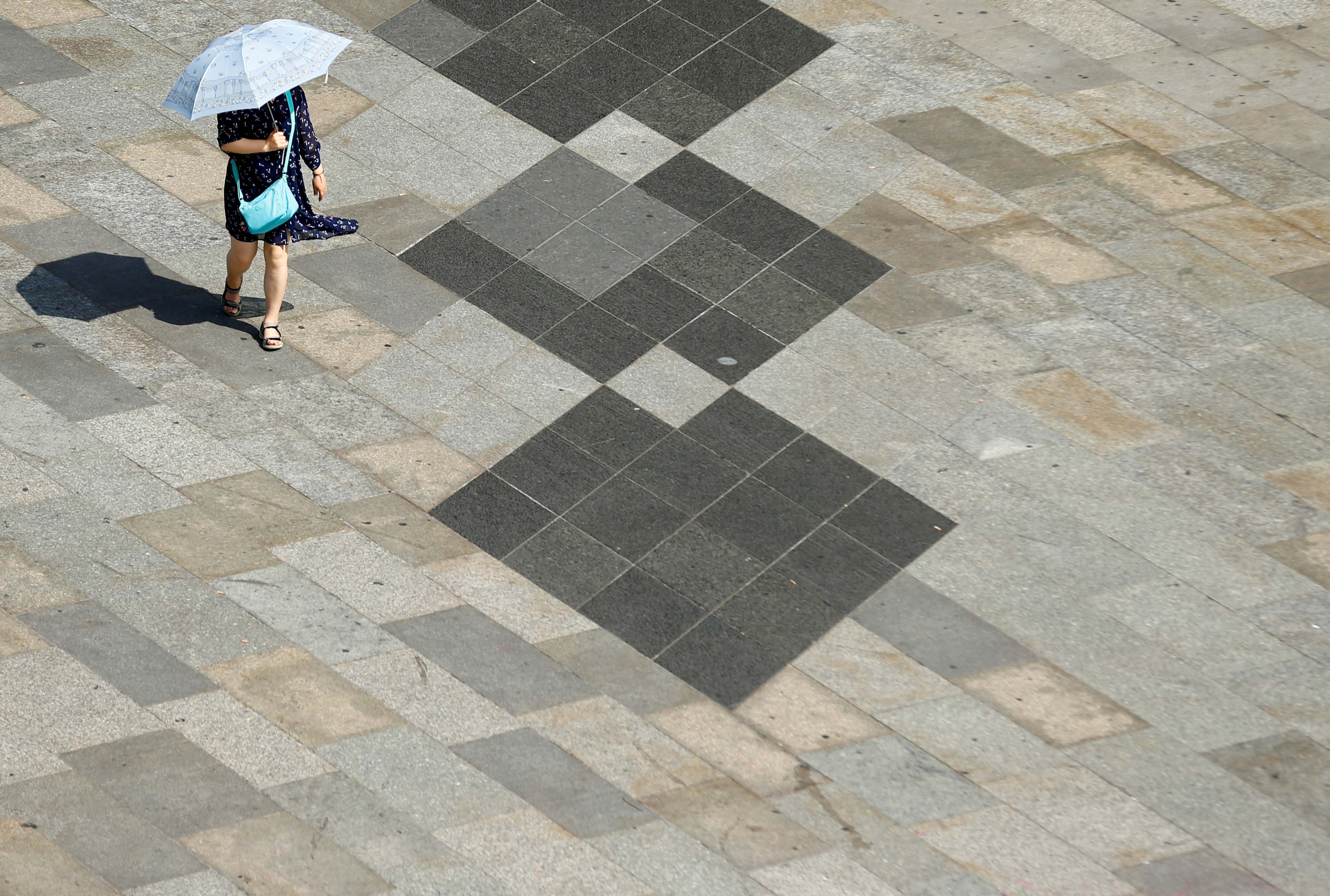 Eine Frau schützt sich an einem heißen Sommertag in Köln mit einem Regenschirm vor der Sonne, Deutschland, 25. Juli 2019.