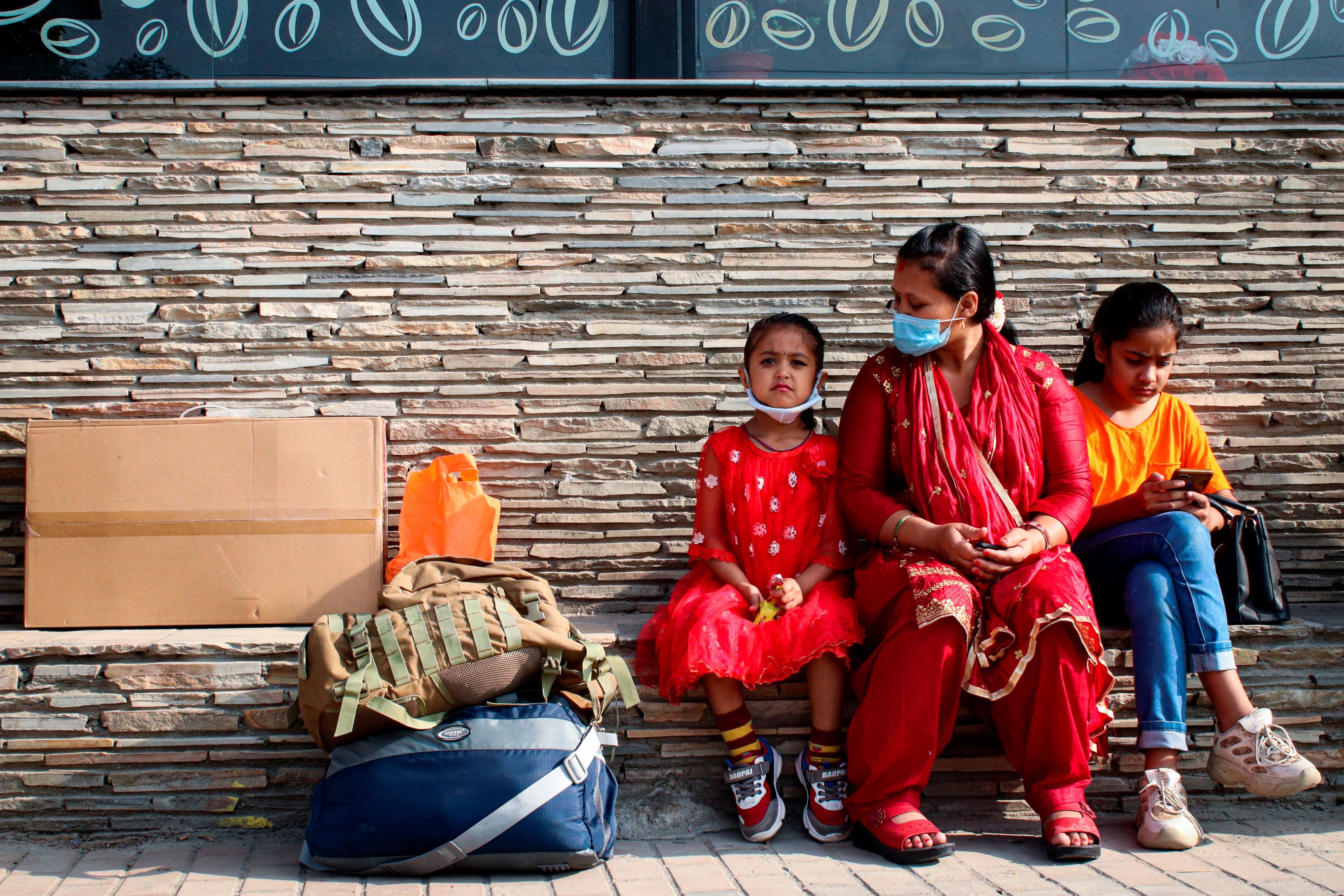 A woman and two young girls sit at a bus station