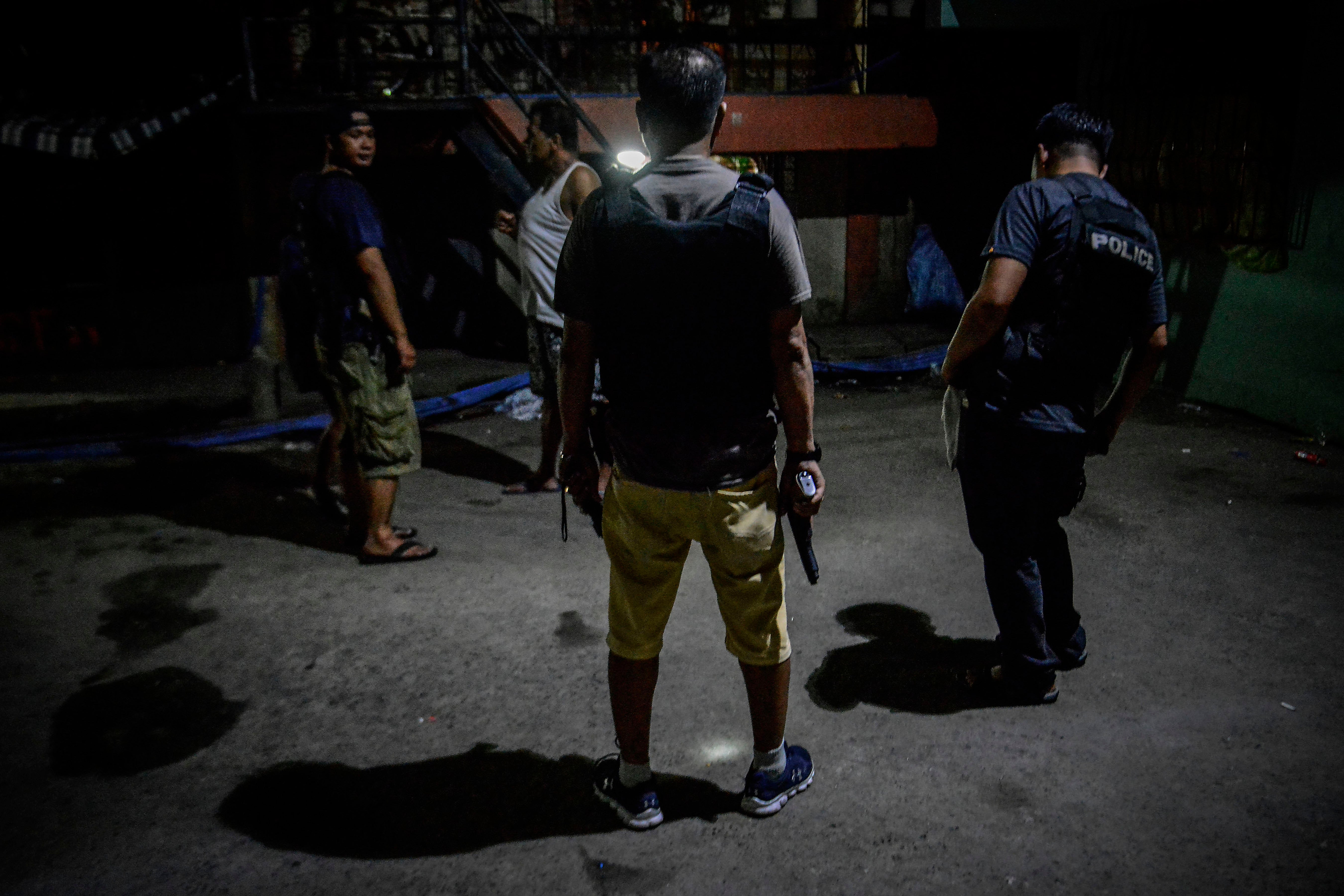 Policemen in plainclothes patrol a dark alley near the scene where three men were killed during a police anti-drug operation in Caloocan, Metro Manila, Philippines. 