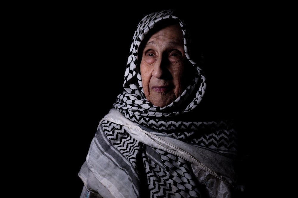 A photo of an older woman wearing a keffiyeh as a headscarf.