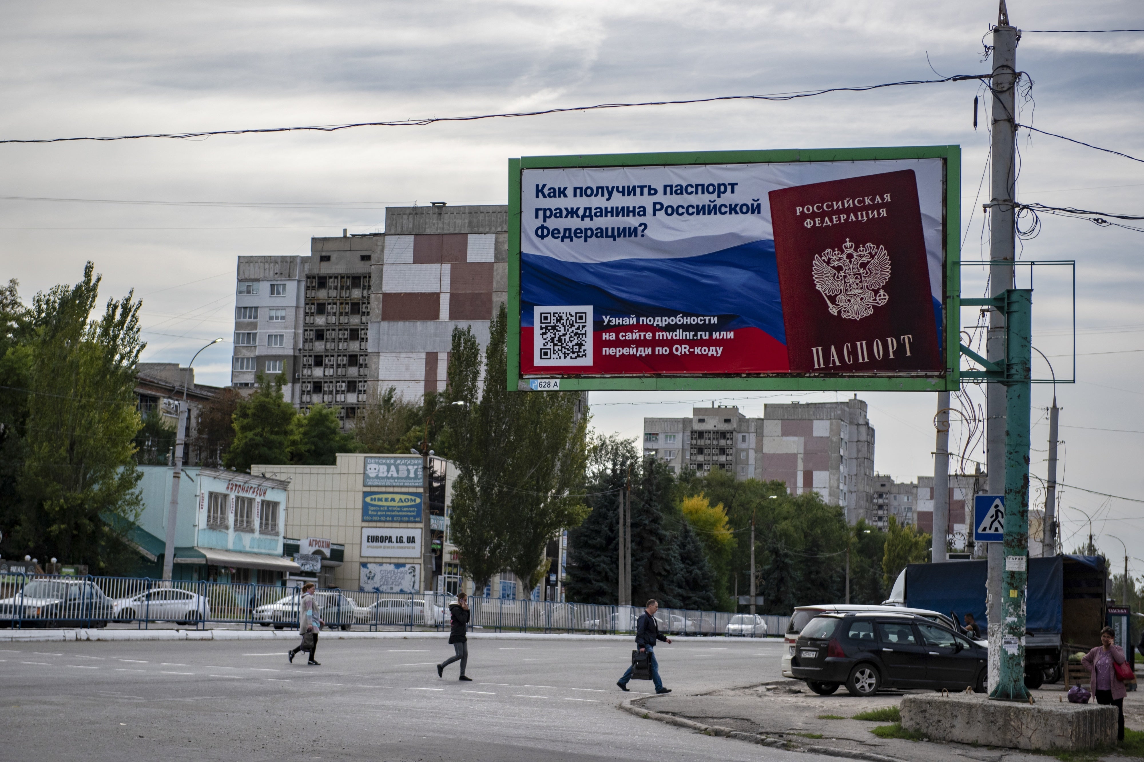 People cross a street with a billboard reading "How to get a passport of a citizen of Russia" in the occupied territory of Luhansk, September 22, 2022.