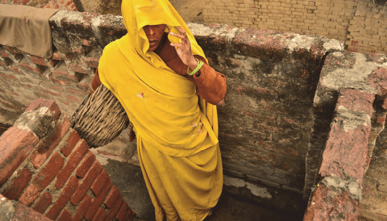 "Eine Dalit entfernt Exkremente aus einer Toilette im Dorf Kasela in Uttar Pradesh, Indien. Dort versagt die Regierung dabei, die Gesetze umzusetzen, durch die verboten ist, dass Toiletten per Hand entleert werden."