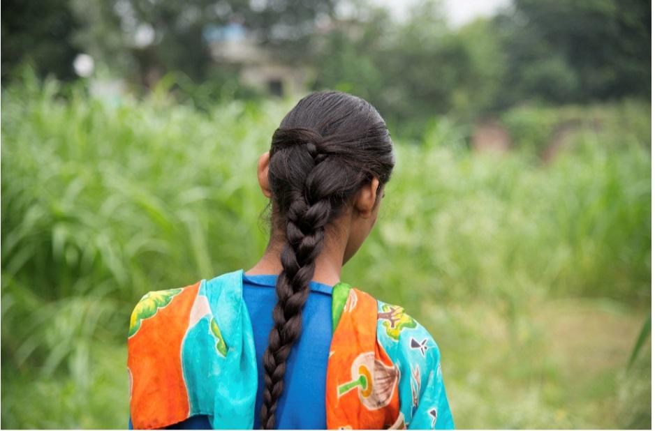 A young girl with long hair portraid from behind, in front of a field. 