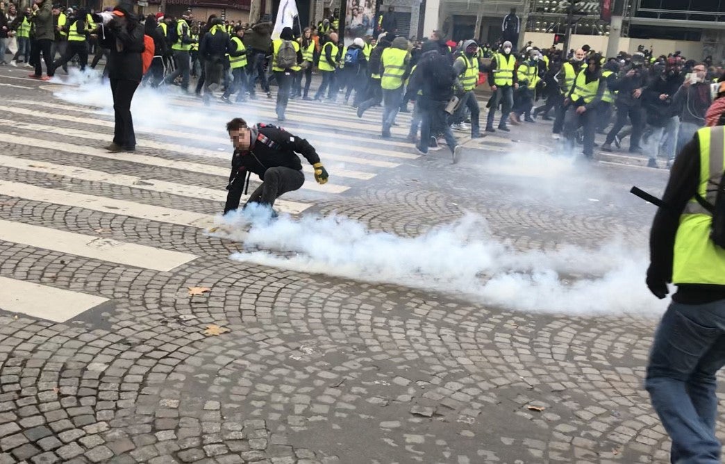 Protester picks up a tear gas grenade during a police charge on December 8, 2019 on the Champs Elysees, Paris.