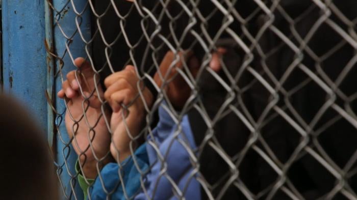 A child's hands holding onto fence