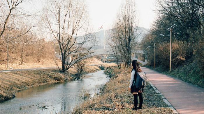 A schoolgirl stands next to a stream 