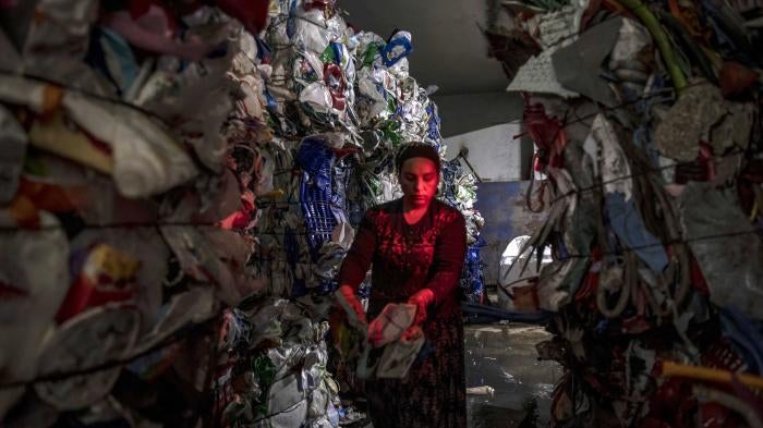 A woman stands between piles of plastic