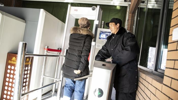 A Chinese security officer watches a woman pass through a checkpoint, equipped with a metal detector and facial recognition technology, to enter the main bazaar in Urumqi in the Xinjiang region of China.