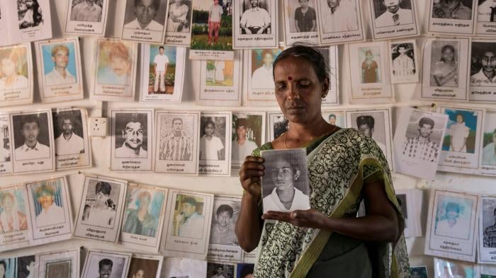 A woman holds a framed photo in front of a wall of other photos