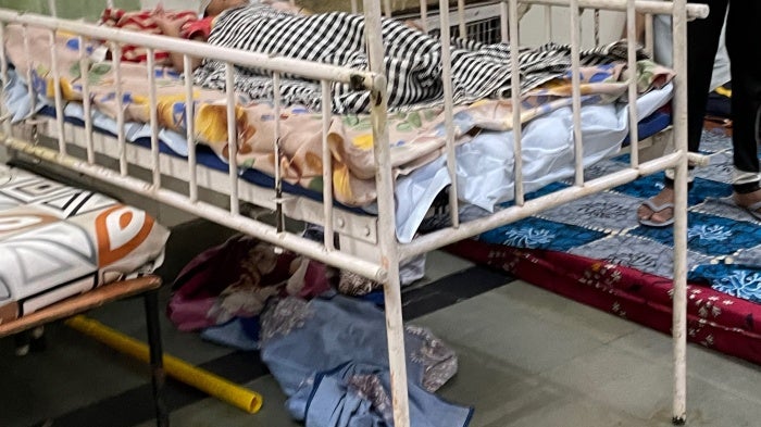 An individual lying in a metal-framed bed inside the Asha Kiran institution.