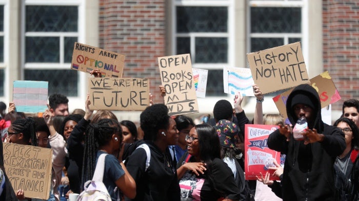 A group of high school students hold signs in front of a school building