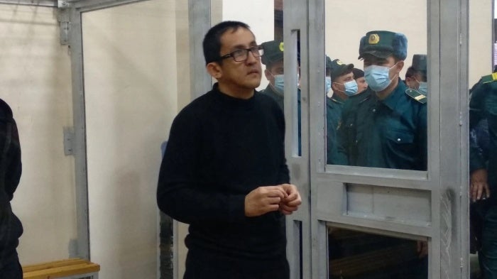 A man stands inside a glass defendants cage in a courtroom
