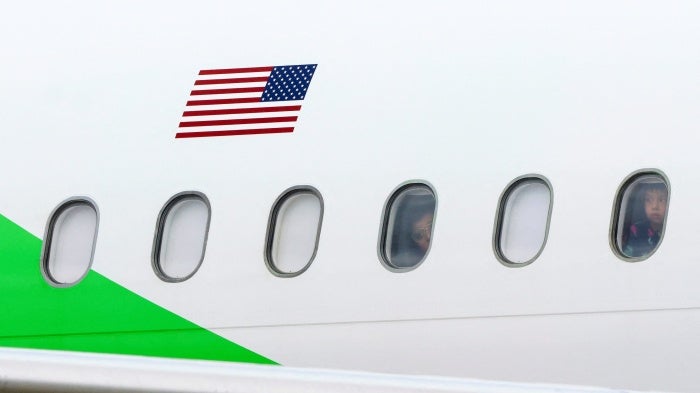 Migrants look out the windows of a plane