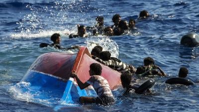 Migrants swim next to their overturned wooden boat 