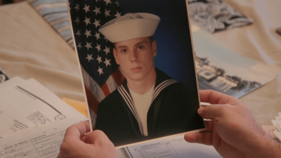 A man holds a picture of himself in Navy uniform