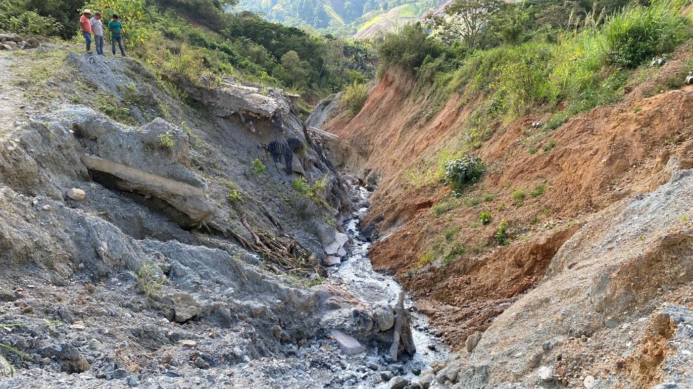  Men peer out over the remains of a portion of the road that had connected the town of Timushan to La Unión, Zacapa state, Guatemala. The road was destroyed during Eta and Iota in November 2020, and has not yet been rebuilt, March 2022.
 © 2022 Max Schoening for Human Rights Watch