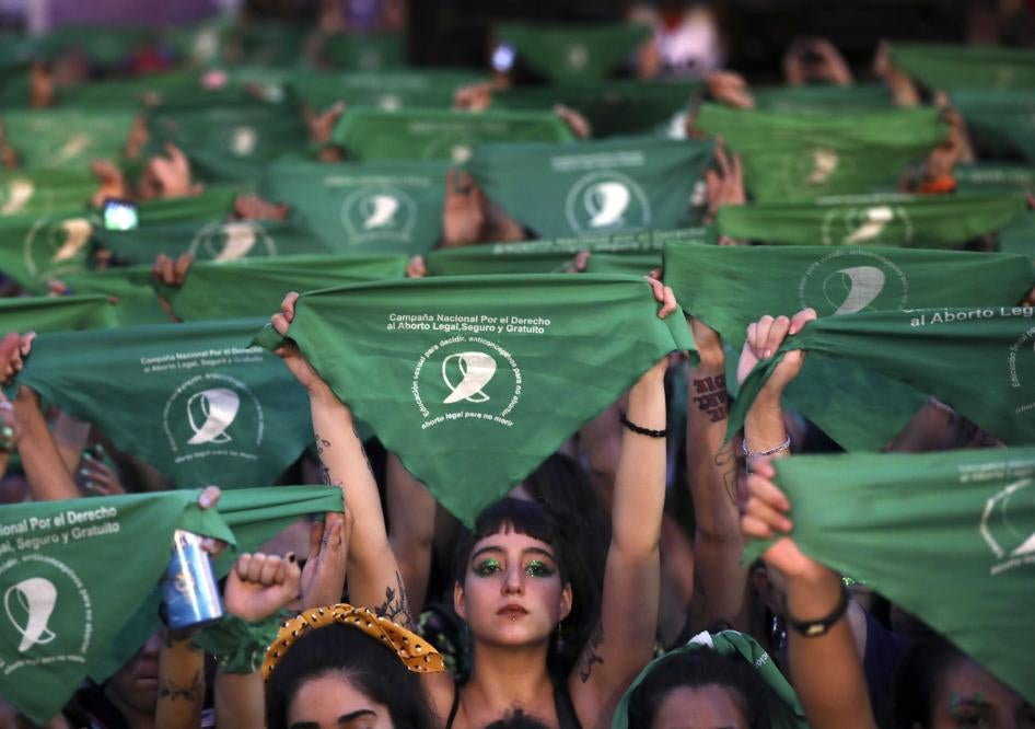 A crowd of women hold up green protest signs