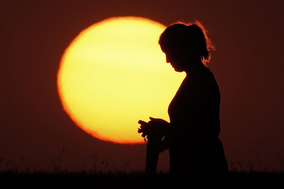 A woman stands in front of a setting sun