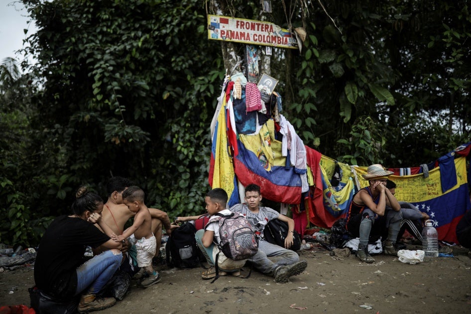 Migrants sit under a sign marking the Panama-Colombia border