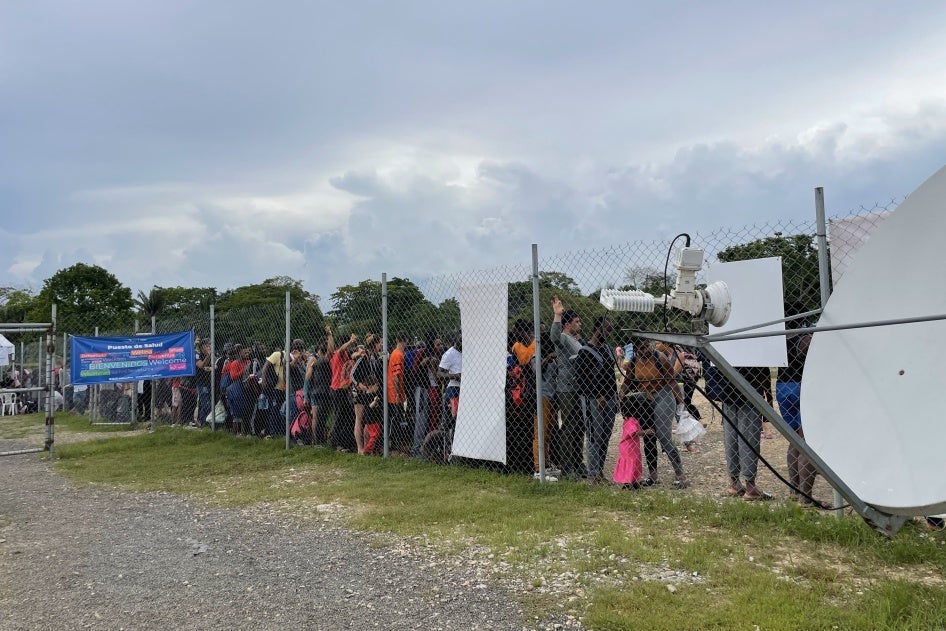 Migrants and asylum seekers wait behind a wire fence