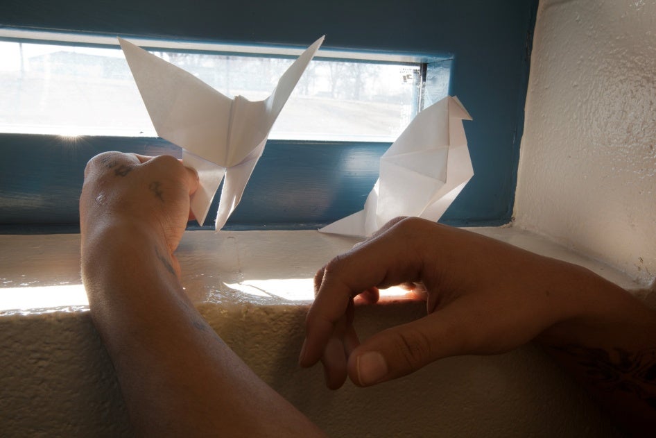 A youth holds two pieces of paper origami in a cell