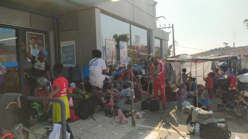 A group of people wait outside a building with their possessions