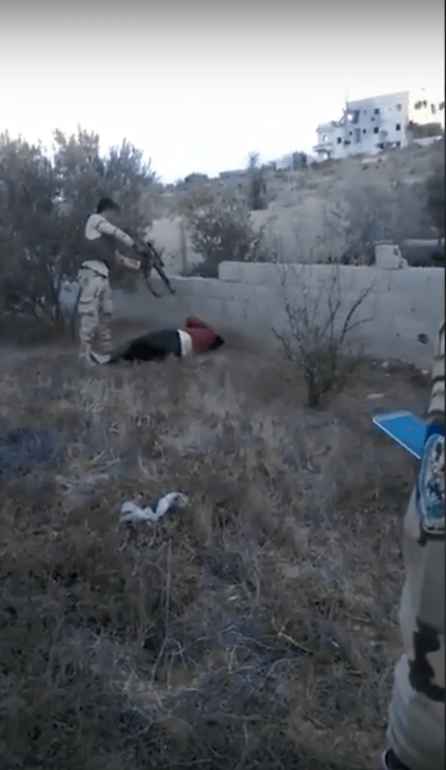 A member of a military-backed militia executes a detainee while being observed by a man (R) wearing an Egyptian military intelligence patch.