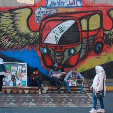 Protesters read copies of newspapers in front of graffiti in Tahrir Square, Baghdad, Iraq, November 20, 2019.