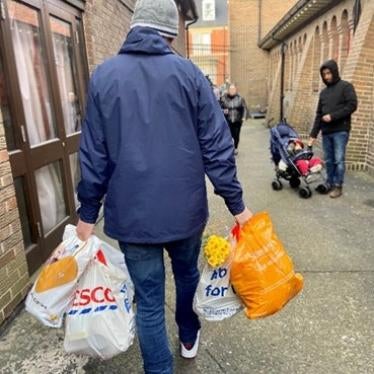 A man in a coat walks down a street carrying grocery bags