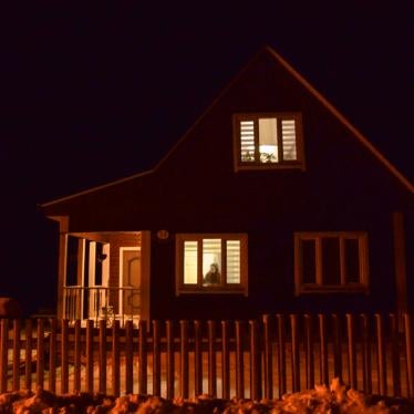 Yulia Alsheuskaya looking through the window of her house outside of Minsk, which she shares with her husband Siarhei who is currently in detention, January 2021.