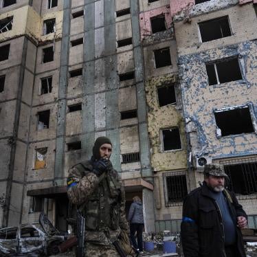 A soldier smokes a cigarette while walking next to a destroyed building