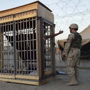 A detainee in an outdoor solitary confinement cell talks with a military police officer at the Abu Ghraib prison on the outskirts of Baghdad, Iraq, June 22, 2004. 