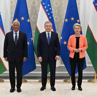 2 men and 1 woman pose for a photo in front of EU and Uzbekistan flags
