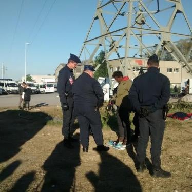 After police halted an evening distribution of food and clothing, three officers stop and question a boy who had paused to change his shoes before returning to the wooded area where he and other migrants spend the night, May 2017. © 2017 Help Refugees