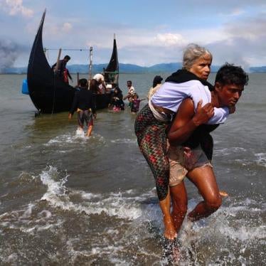 Smoke is seen on Myanmar's side of border as an old Rohingya refugee woman is carried after crossing the Bangladesh-Myanmar border by boat through the Bay of Bengal in Shah Porir Dwip, Bangladesh, September 15, 2017. 