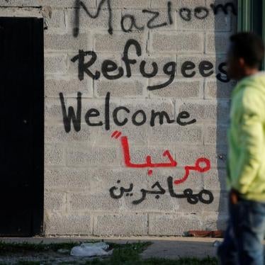 A migrant walks past the slogans which read "refugees welcome" written on a wall near the former "jungle" in Calais, France, August 23, 2017. 