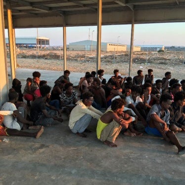 Rescued migrants sit on a coast some 100 kilometers (60 miles) east of Tripoli, Libya